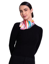 A woman wearing A square silk scarf featuring a vibrant, multicolored abstract floral and geometric print.