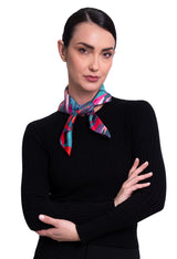 A woman wearing a square silk scarf featuring a vibrant, multicolored abstract floral and geometric print.
