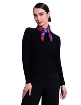 A woman wearing A square silk scarf featuring a vibrant abstract floral and geometric pattern.