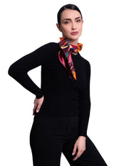A woman modeling A square silk scarf featuring a vibrant abstract floral and geometric pattern.